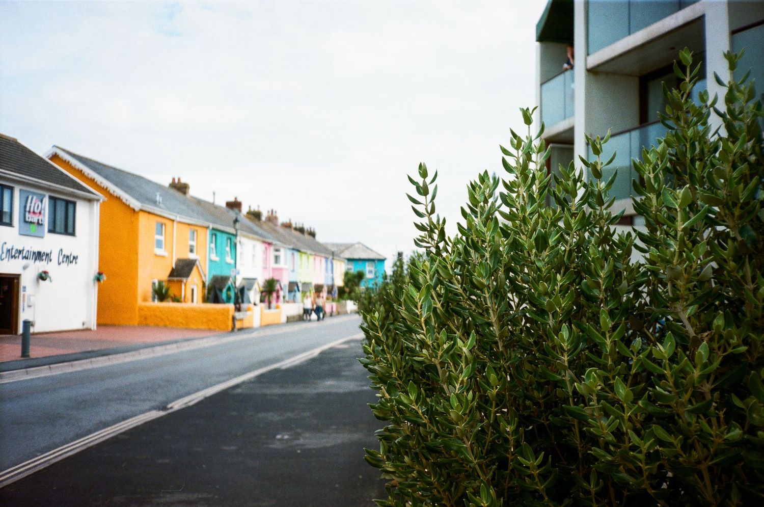 Colorful row houses with orange and pastel facades line a steep street in a coastal town.