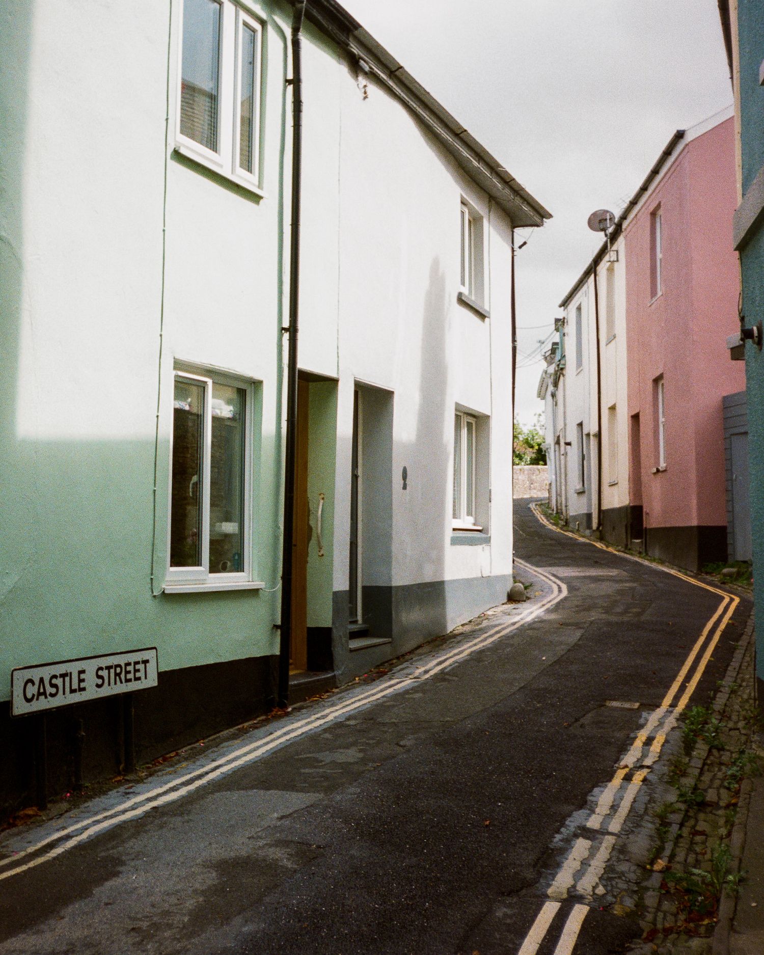 Winding street called Castle Street with white-washed buildings and double yellow lines.