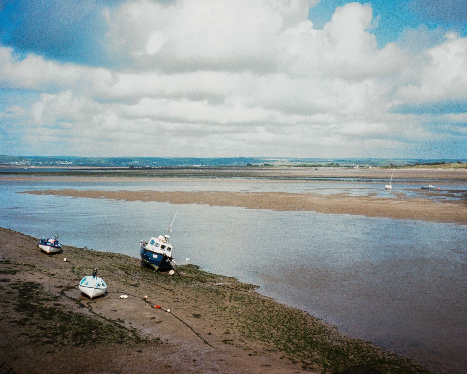 Coastal panorama showing boats anchored in a tidal mudflat during low tide.