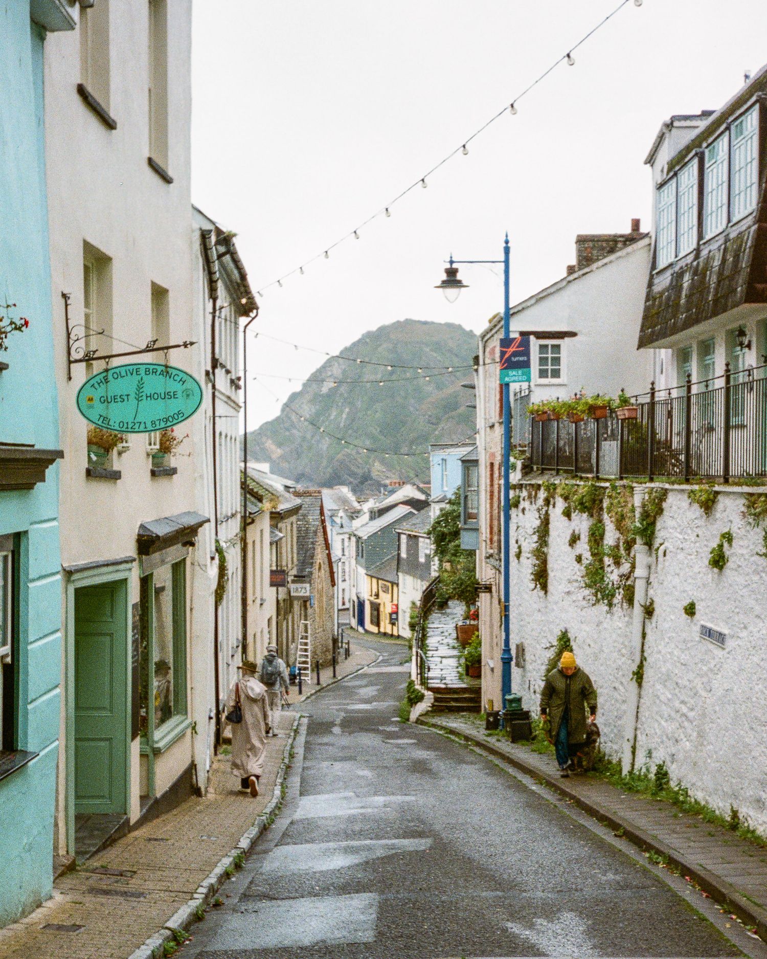 Charming narrow street in a coastal village with whitewashed buildings and a mountain backdrop.
