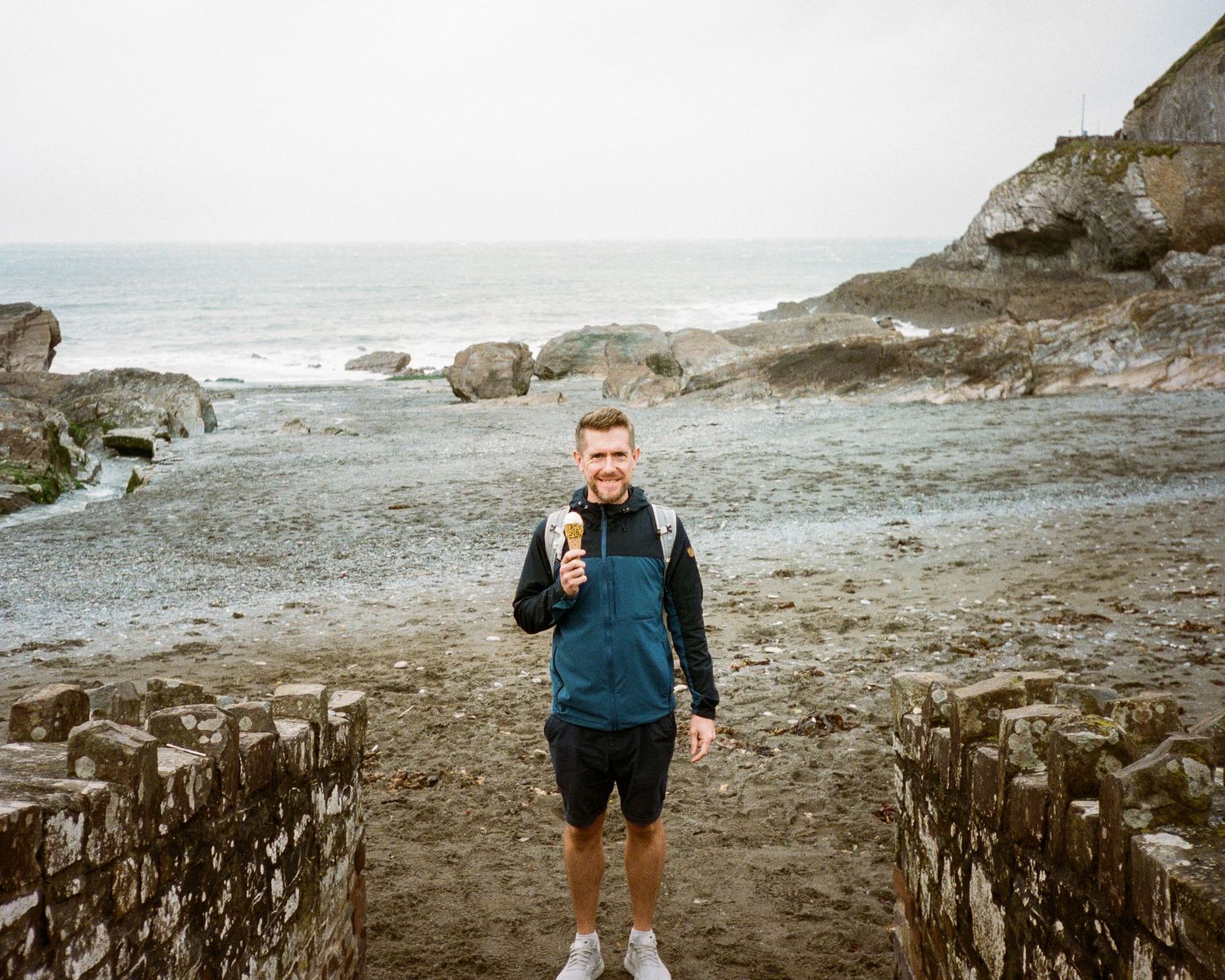 Rocky coastal beach with waves crashing against the shore on an overcast day.