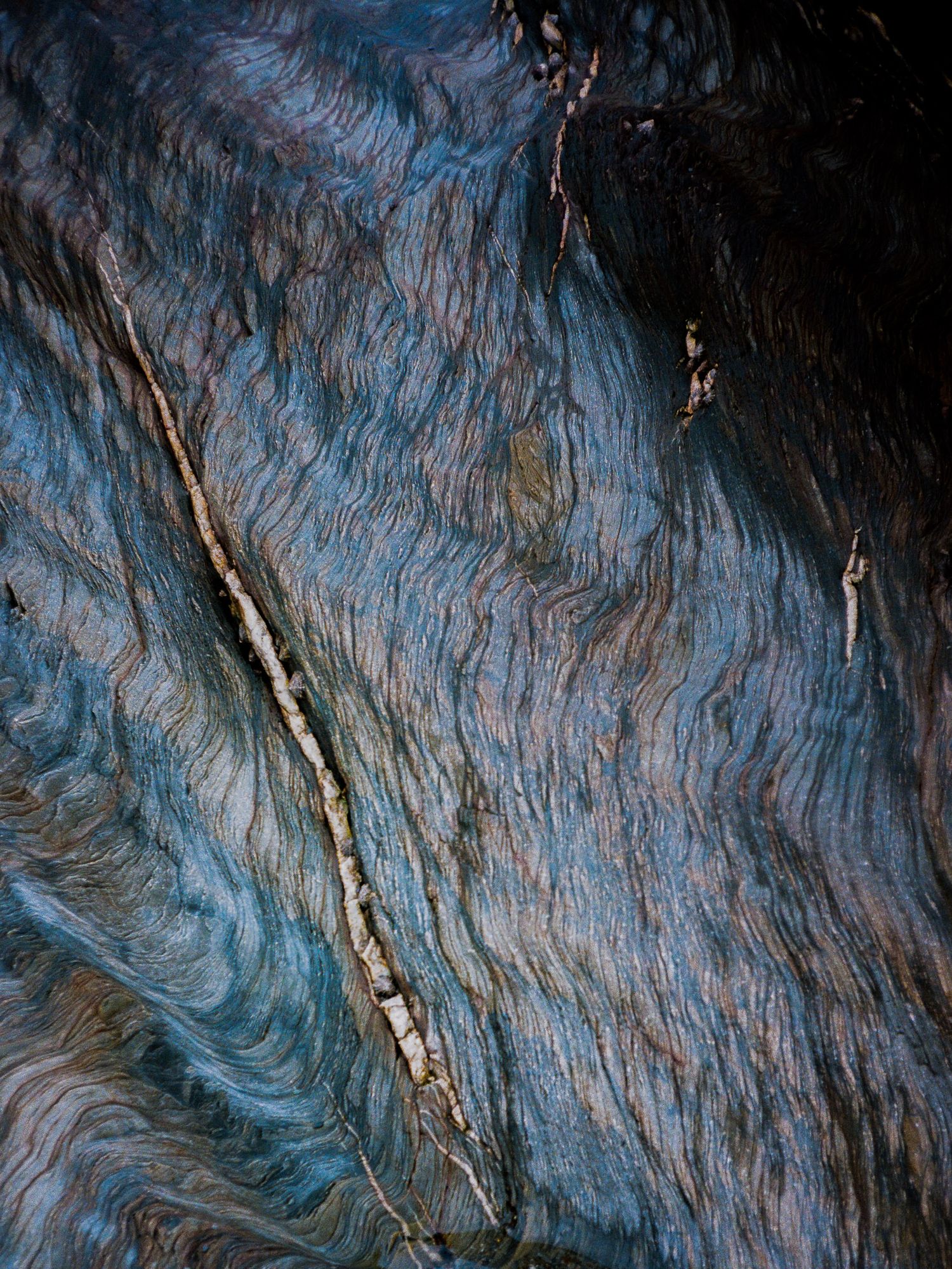 Abstract pattern of blue and silver streaks in weathered rock formation.