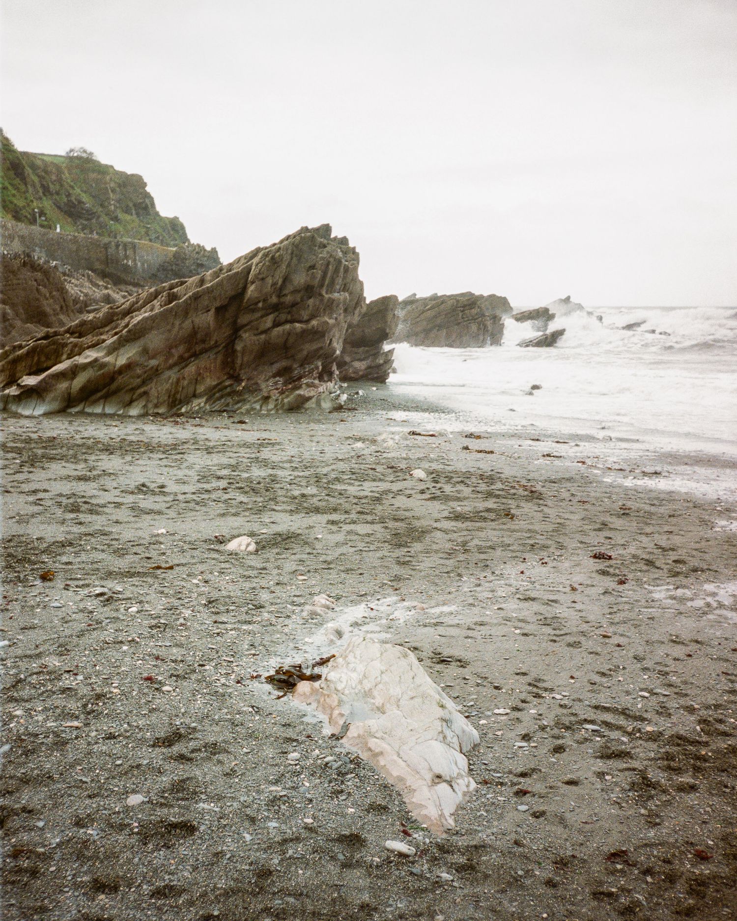 Large rocky outcrop on a misty beach with waves breaking against the shore.