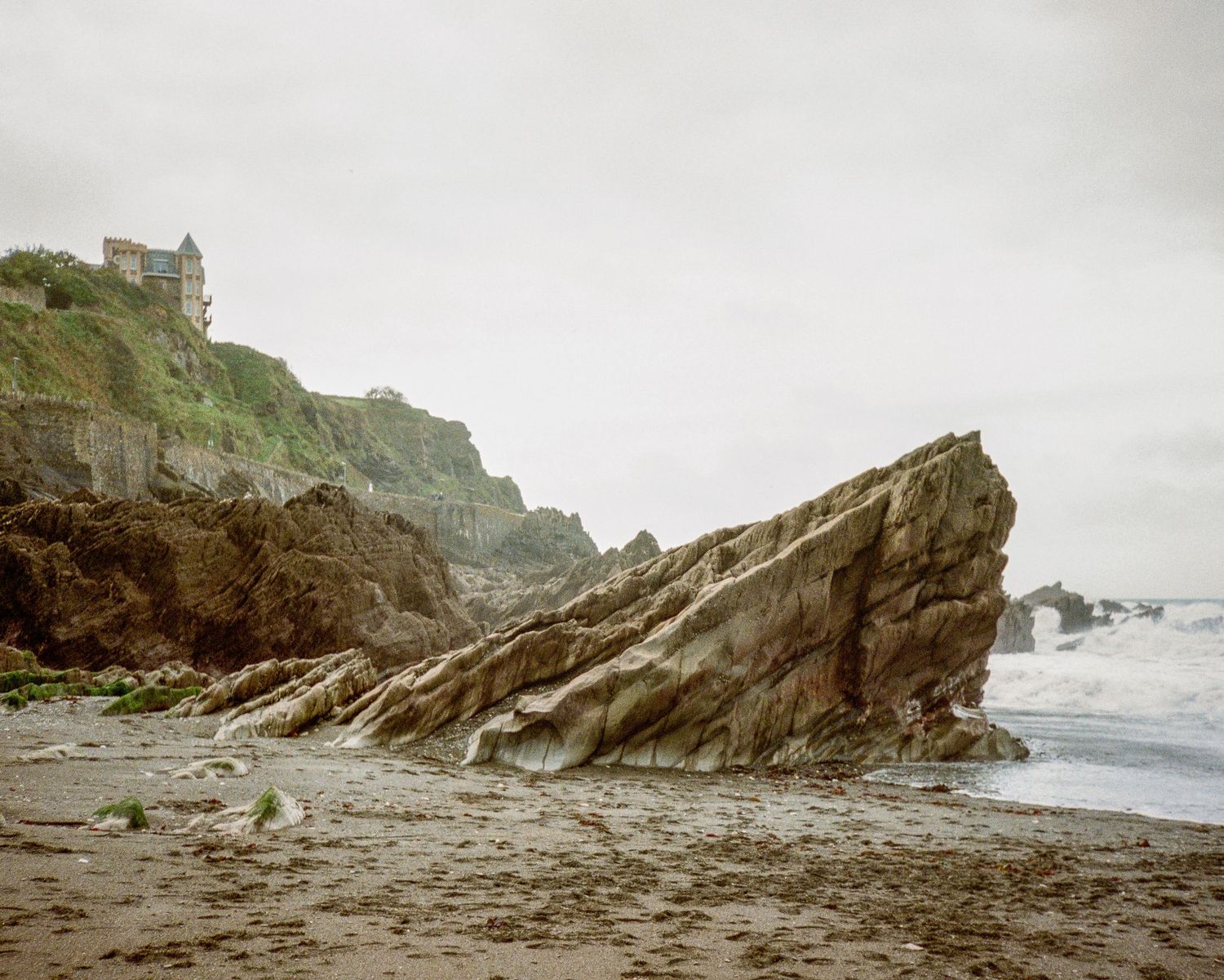 Dramatic angular rock formation jutting out from a coastal beach with cliffs in the background Ilfracombe.