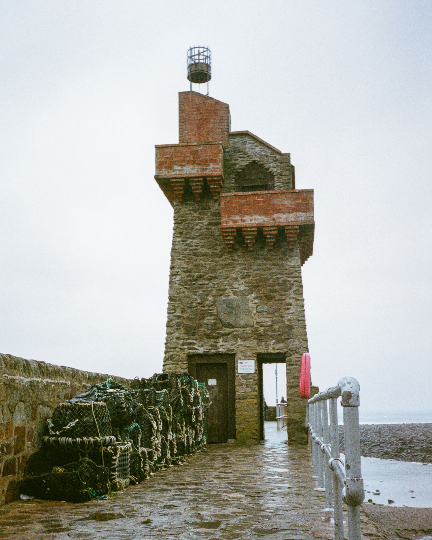 Historic stone lighthouse tower with metal railing along a coastal wall.
