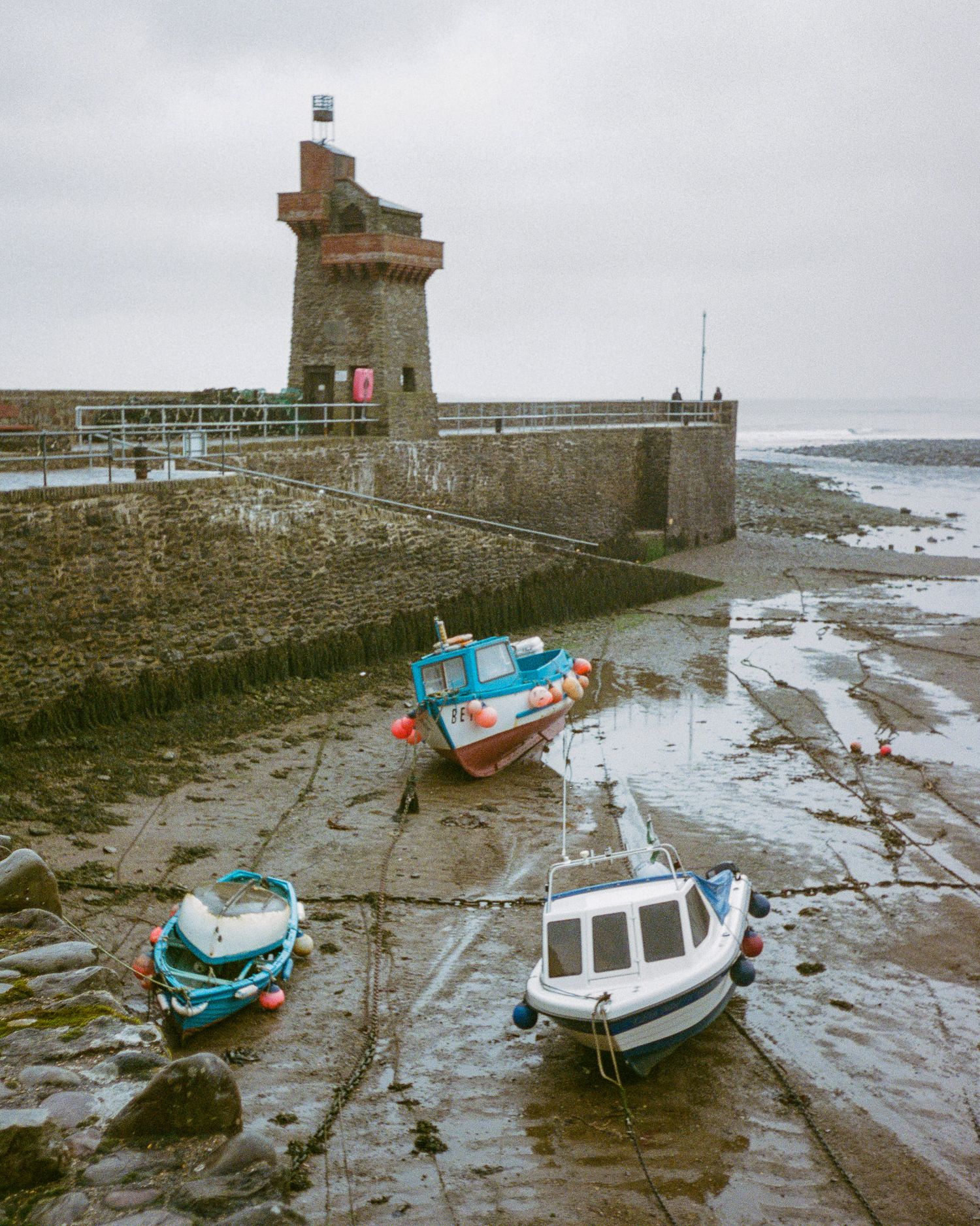 Small fishing boats moored at low tide near a stone lighthouse and harbor wall Lynmouth.