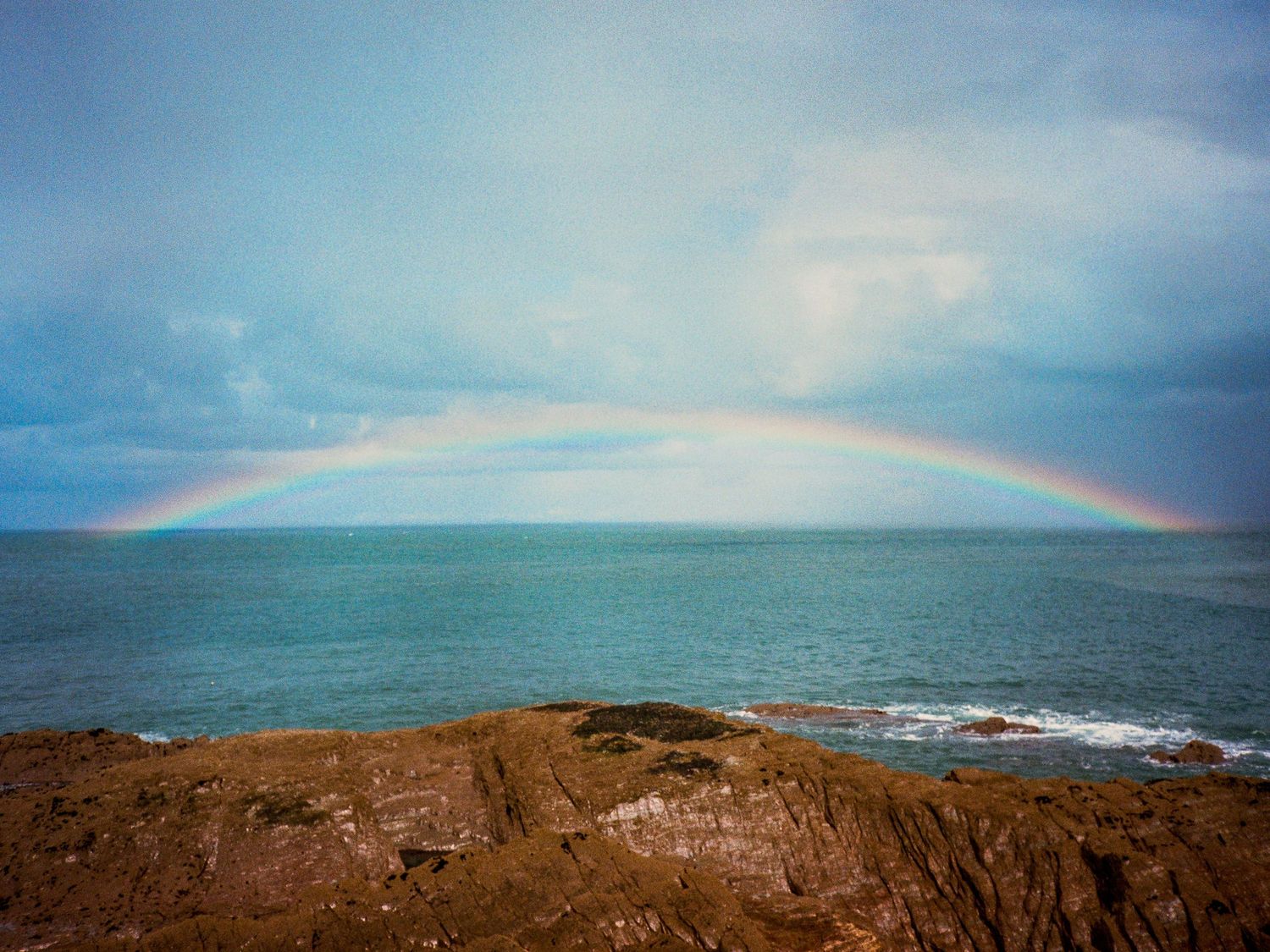 Beautiful rainbow arching over the ocean horizon on a cloudy day.