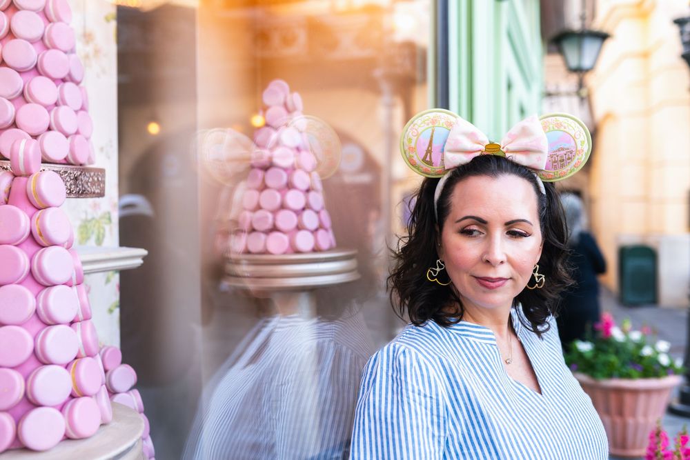 A person wearing a blue and white striped shirt poses near pink macaron towers in a bakery setting.