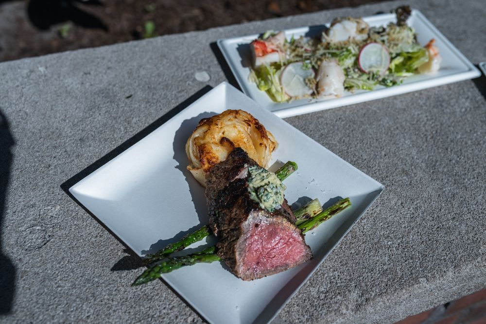 Plated fine dining dishes featuring asparagus and medium-rare steak on white rectangular plates.