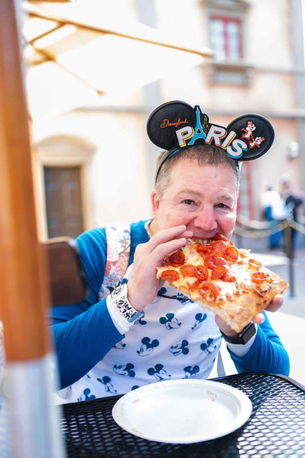 Three sequential photos show someone taking increasingly large bites of a slice of cheese pizza at an outdoor table.