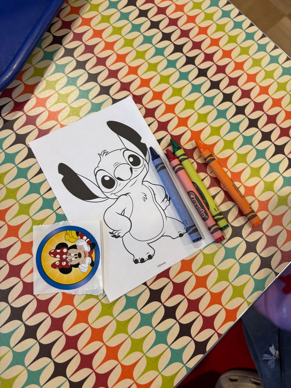 A black and white drawing of Stitch character on colorful patterned paper with a pen and sticker.