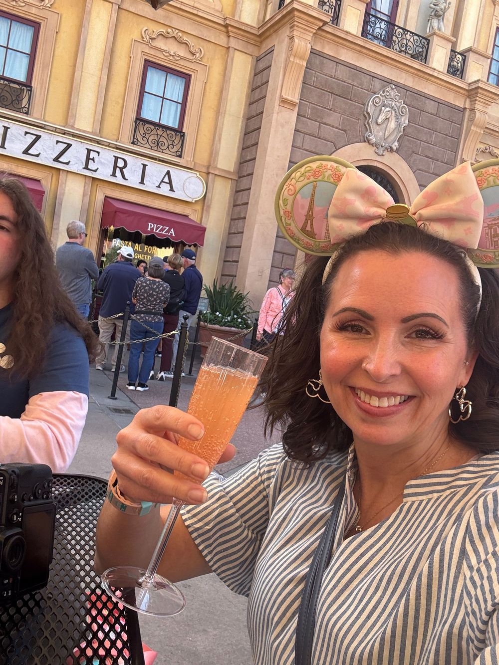 A person enjoying gelato while posing in front of a pizzeria storefront with striped clothing and a hair bow.