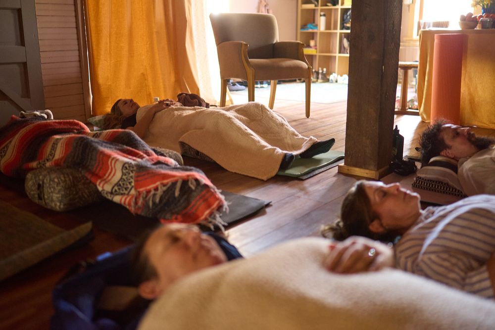 Group of people lying on yoga mats during a restorative meditation session on a wooden floor.