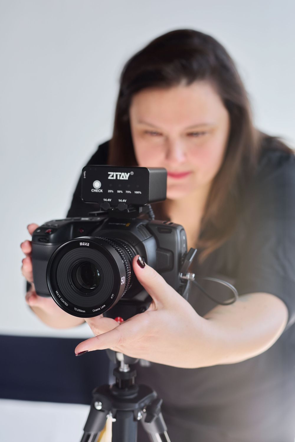 Woman adjusts Zitay camera mounted on tripod in a professional photography studio setting.