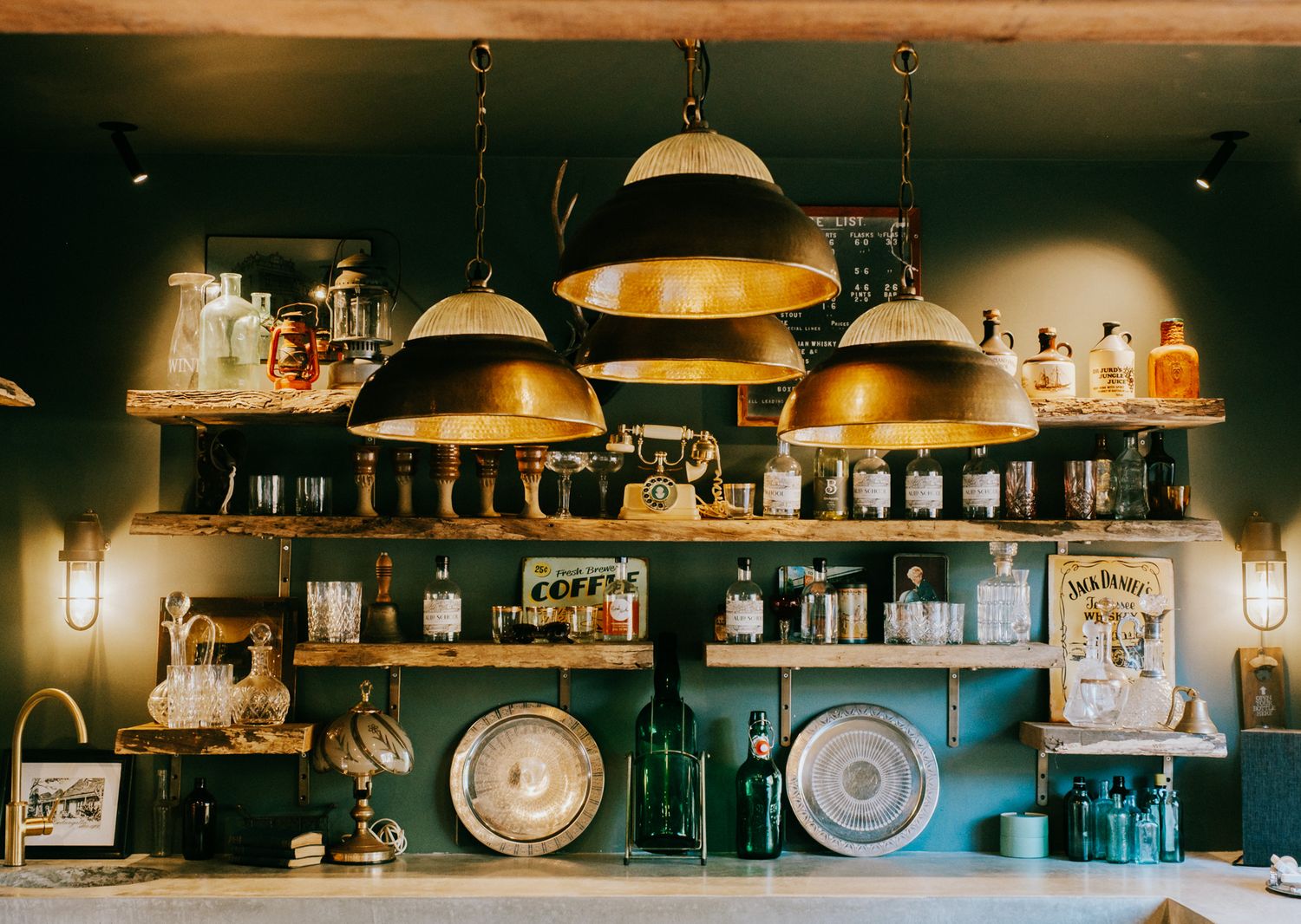 Panoramic view of a cozy bar interior with warm lighting, hanging pendant lamps, and shelves stocked with bottles.