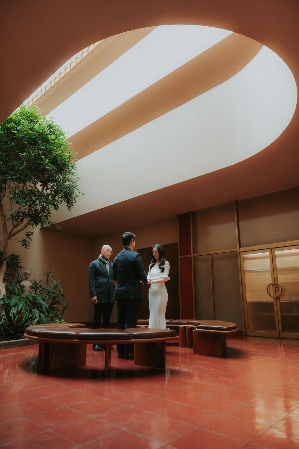 Modern architectural space with diagonal skylights illuminating a red floor and indoor plants.