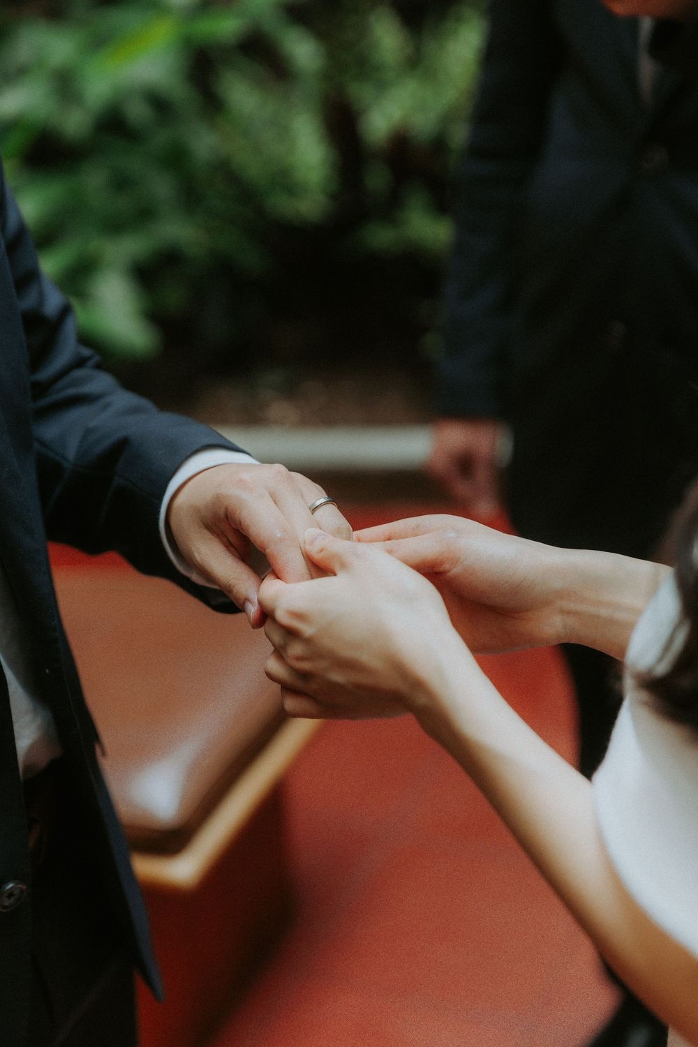A close-up shot of hands exchanging rings during a wedding ceremony against a blurred green background.