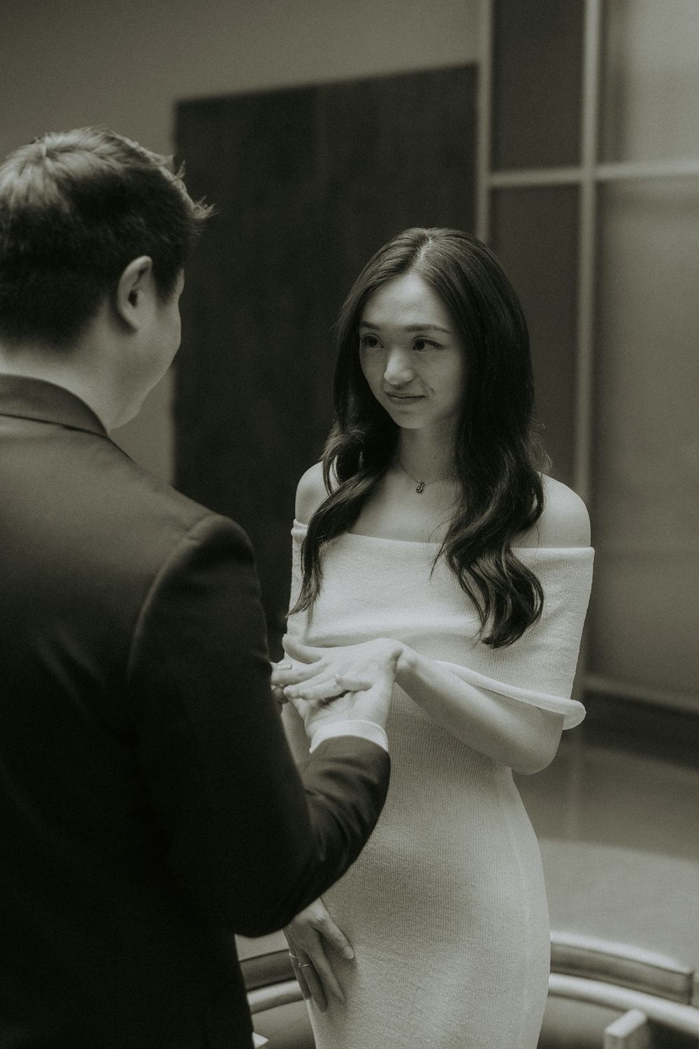 A couple shares a tender moment in a hallway, with the woman wearing an elegant white off-shoulder dress.