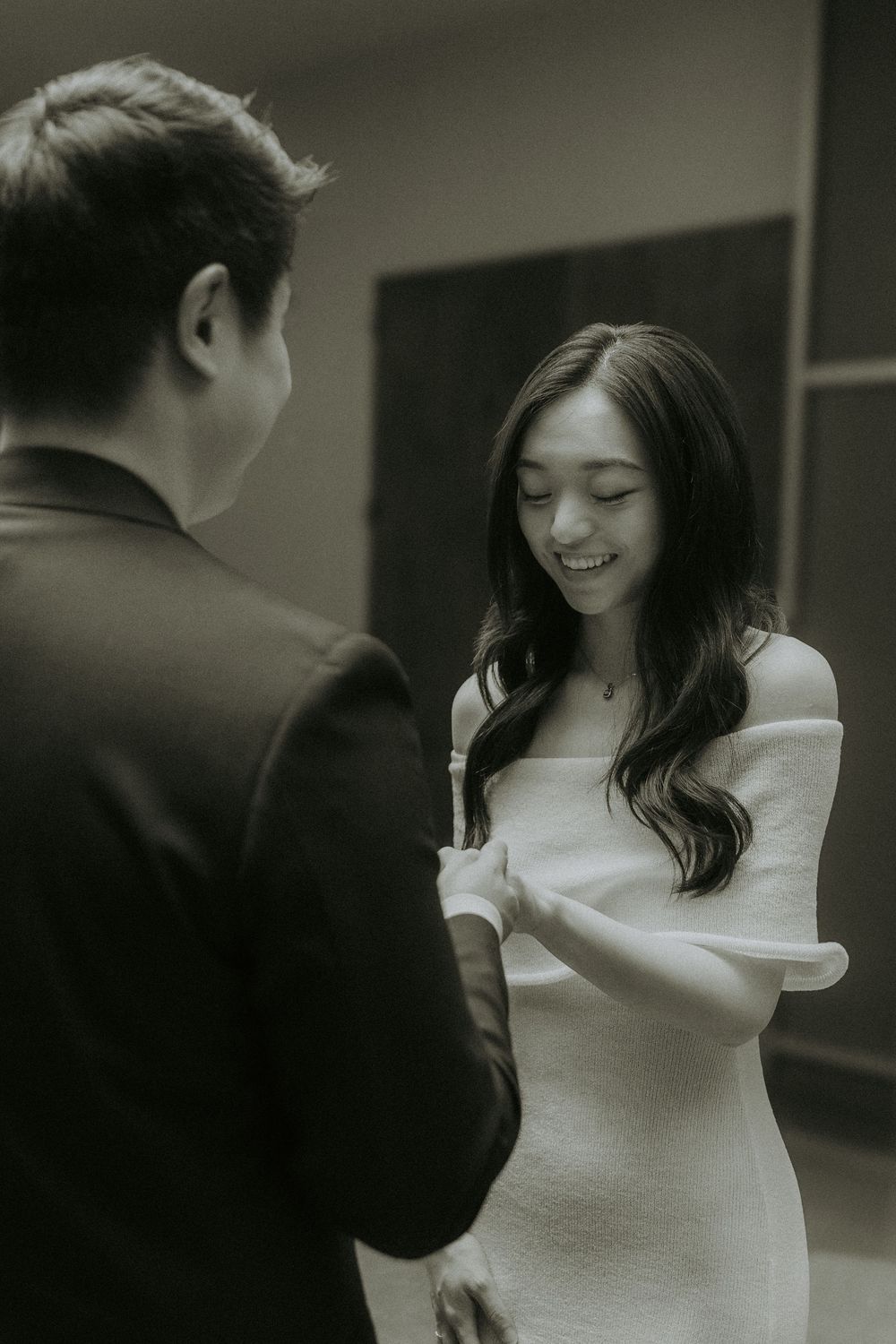 Black and white photo of a couple sharing a joyful moment, with the woman wearing an elegant white off-shoulder dress.