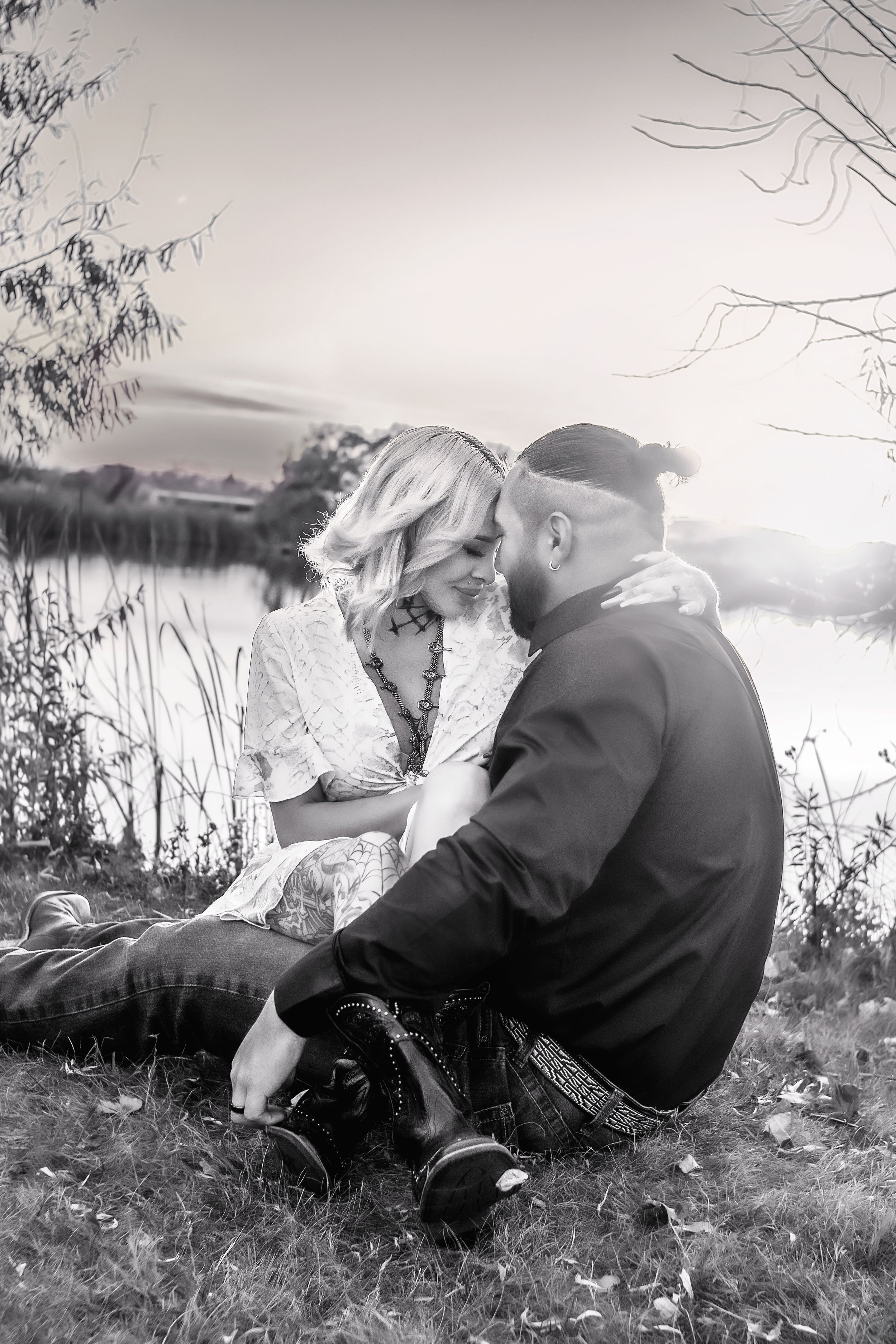 A romantic black and white photo of a couple sitting by a lake during sunset, surrounded by nature in Williston, North Dakota.