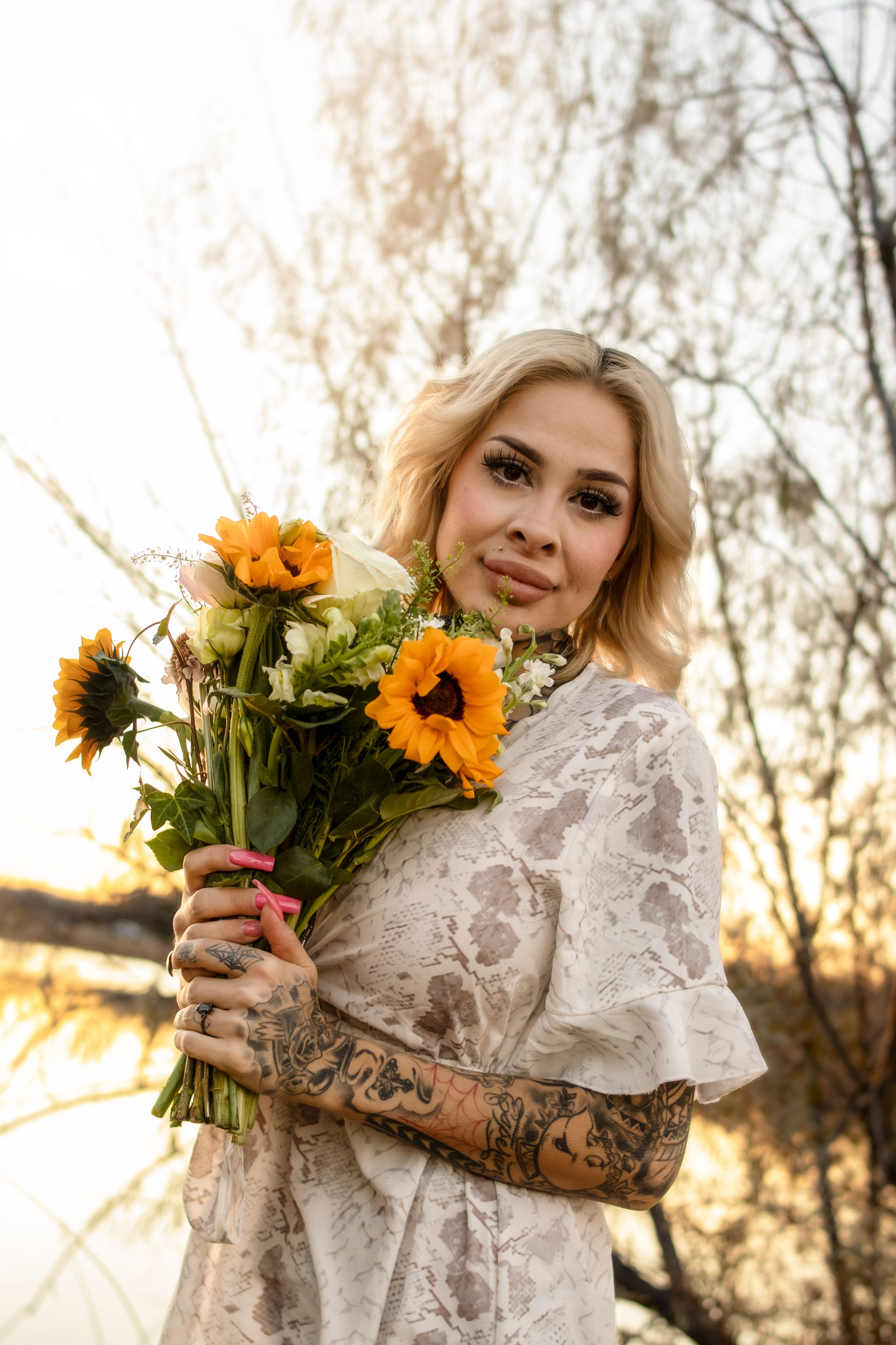 Person in white lace dress holding vibrant sunflowers during golden hour. Taken in Williston, North Dakota.