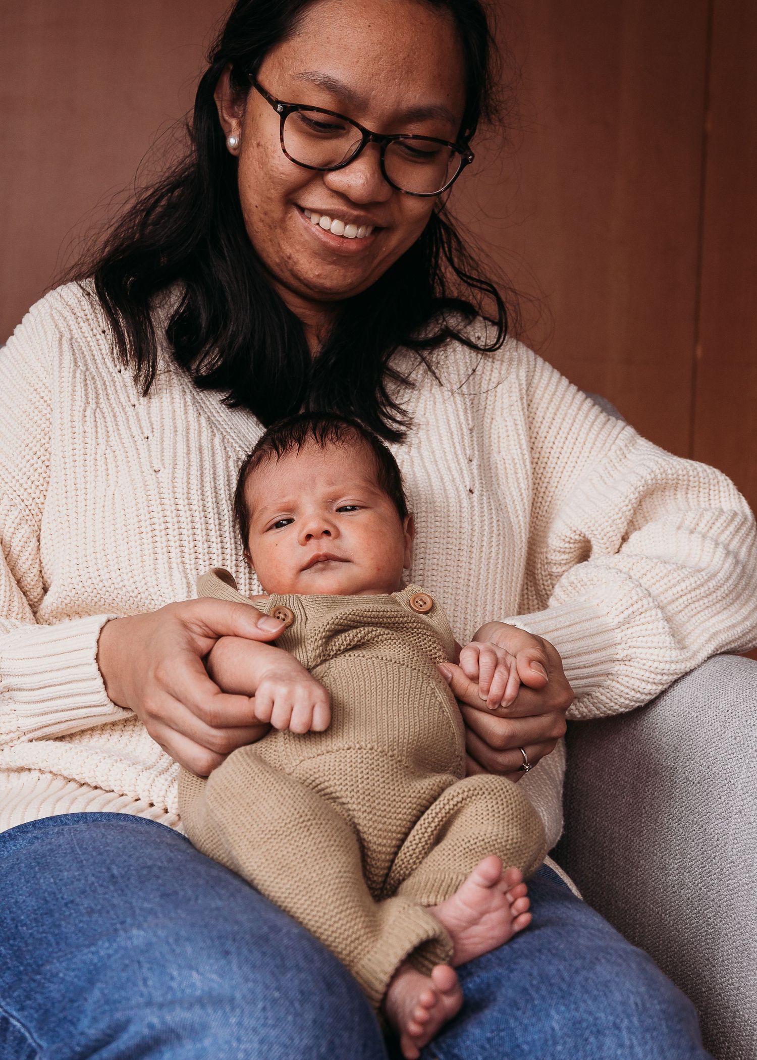A tender moment captured in warm tones as a parent in a white sweater cradles a sleeping baby wearing a beige outfit.