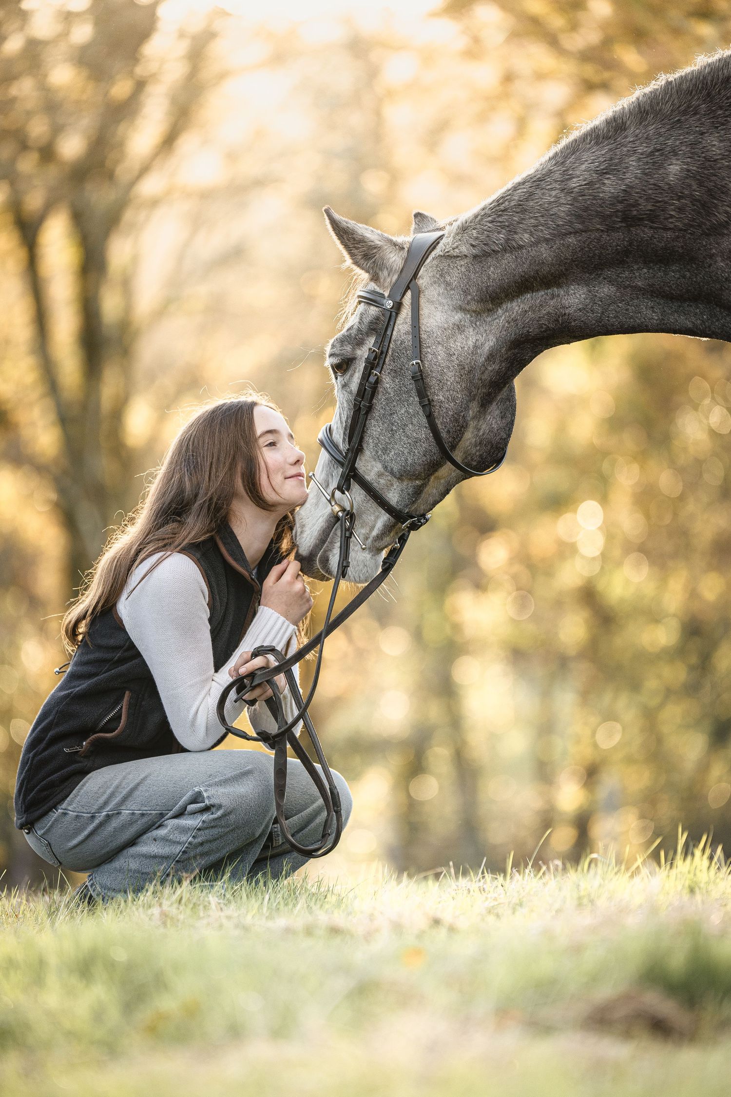 A tender moment between a horse and rider sharing affection in a sunlit autumn setting with bokeh background.