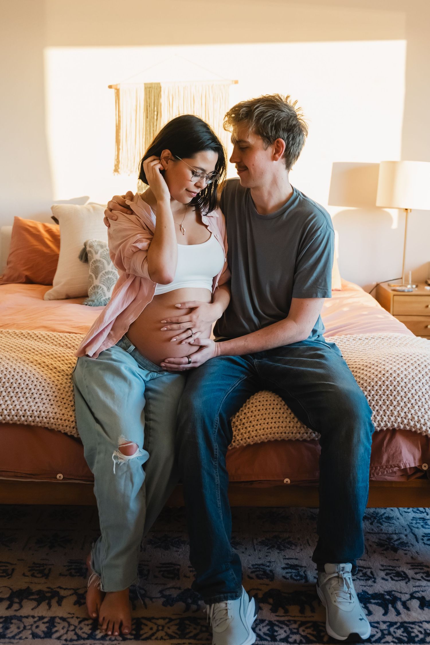 Couple sitting on edge of bed during in-home maternity photos