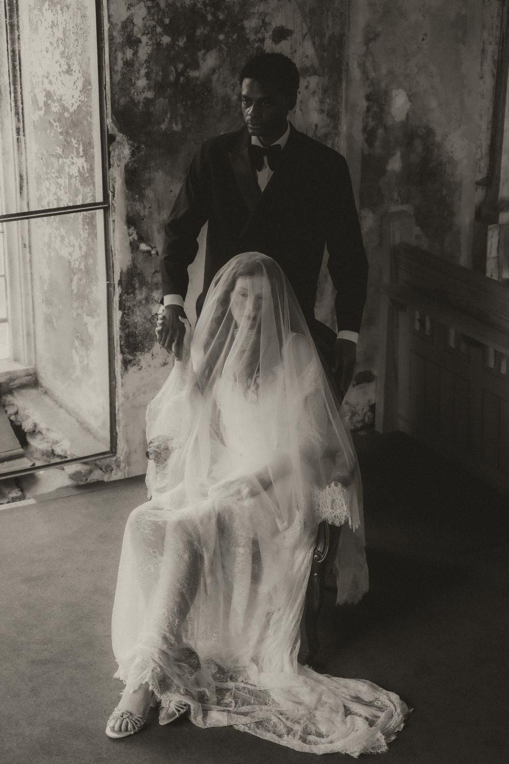 A haunting black and white photograph shows a bride in a flowing veil seated while a figure in dark attire stands behind.