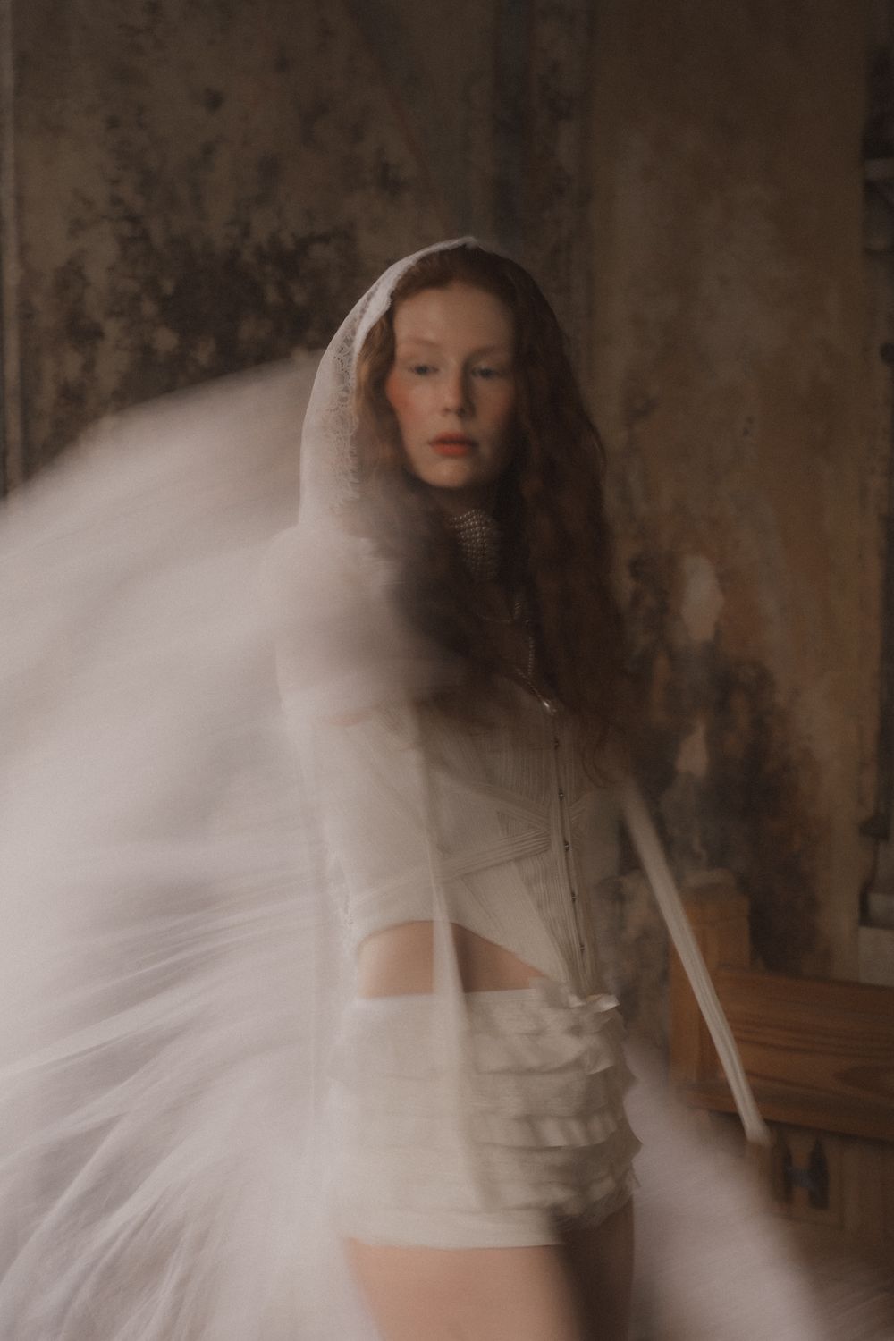 Ethereal figure in white dress creates dreamy motion blur effect against textured wall in artistic portrait series.