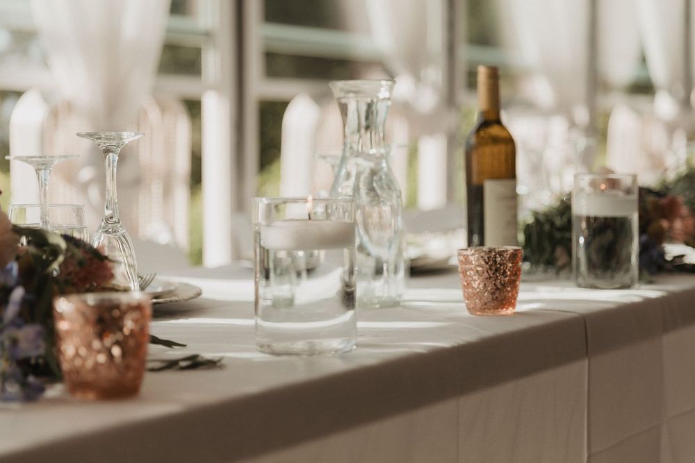 Wedding reception table detail with crystal glassware, water carafe, wine bottle, and copper candle holders.