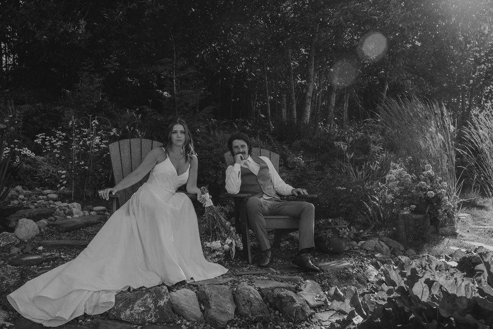Black and white portrait of bride and groom relaxing on chairs in a scenic garden setting.