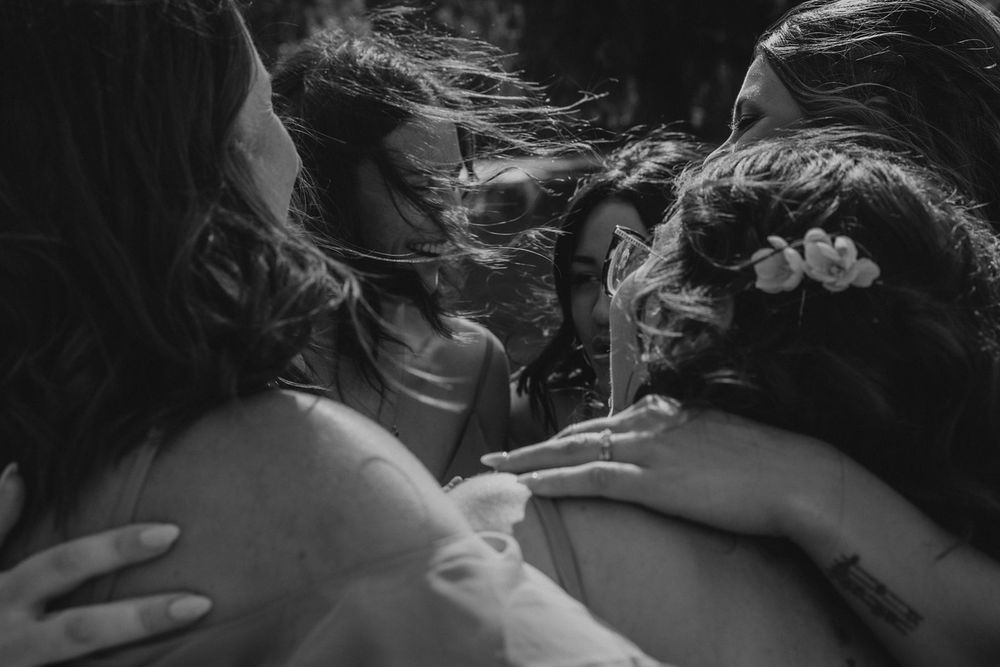Black and white close-up of bride sharing an emotional group hug with bridesmaids at wedding.