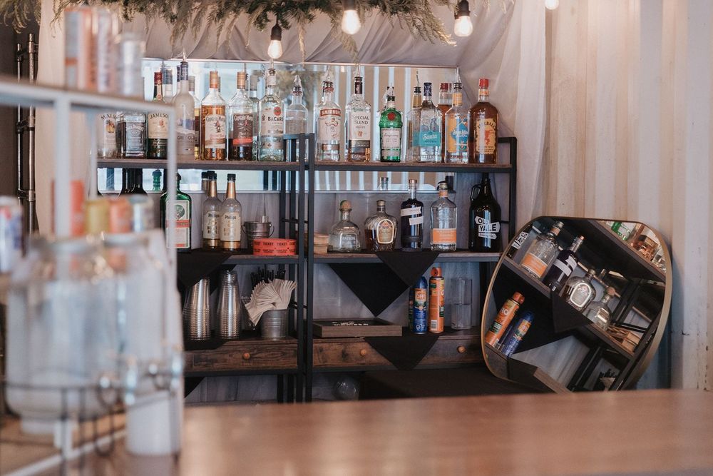 Rustic wedding bar setup with shelves of liquor bottles and cocktail supplies at a reception venue.