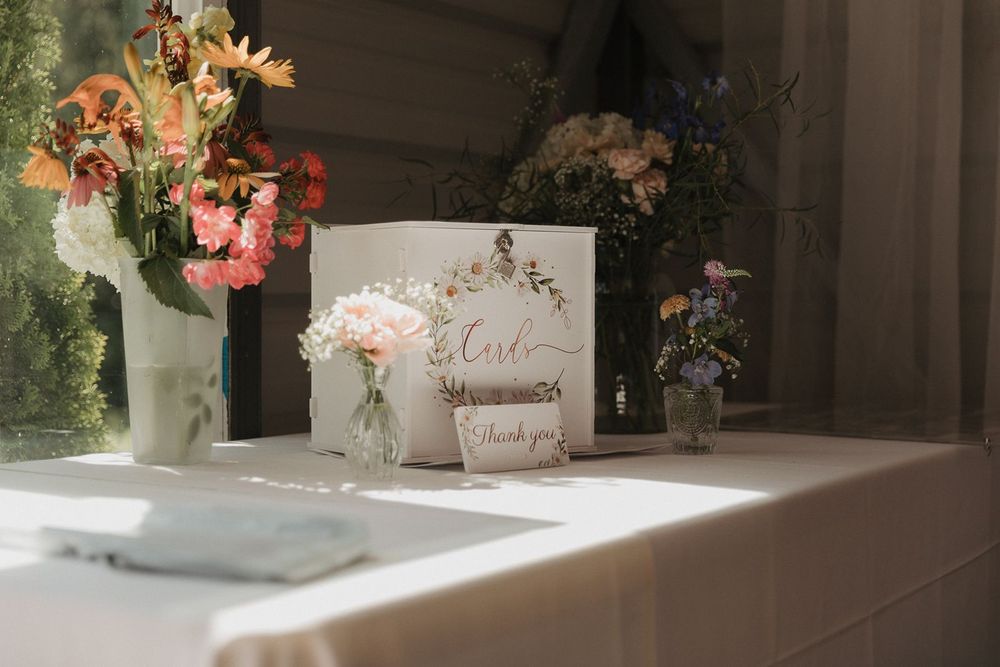 Elegant wedding card table with floral arrangements and a decorative thank you sign near a sunlit window.