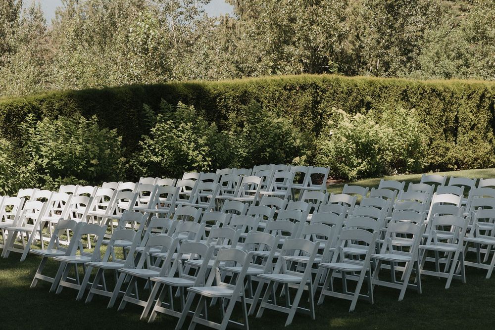 Rows of white folding chairs set up on a lawn for an outdoor wedding ceremony with lush green hedges.