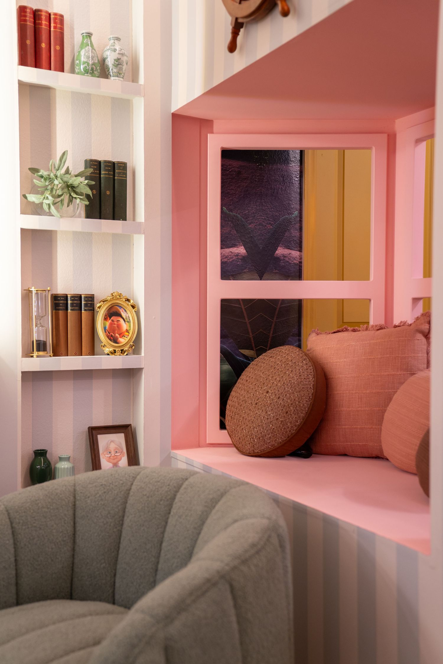 Pink and white built-in shelving unit with decorative glass bottles and a grey scalloped couch in a cozy interior space.