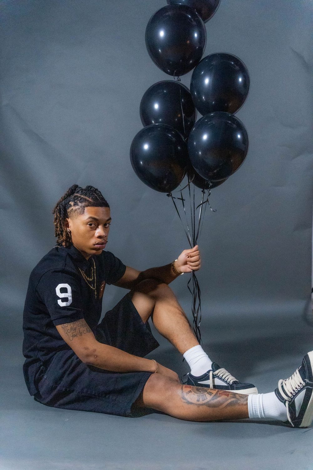 Artistic photo series showing person in black hoodie posing with black balloons against gray backdrop in multiple poses.