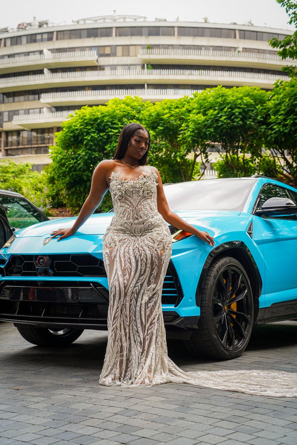 A person in a sparkly white gown poses elegantly next to a bright turquoise luxury sports car.