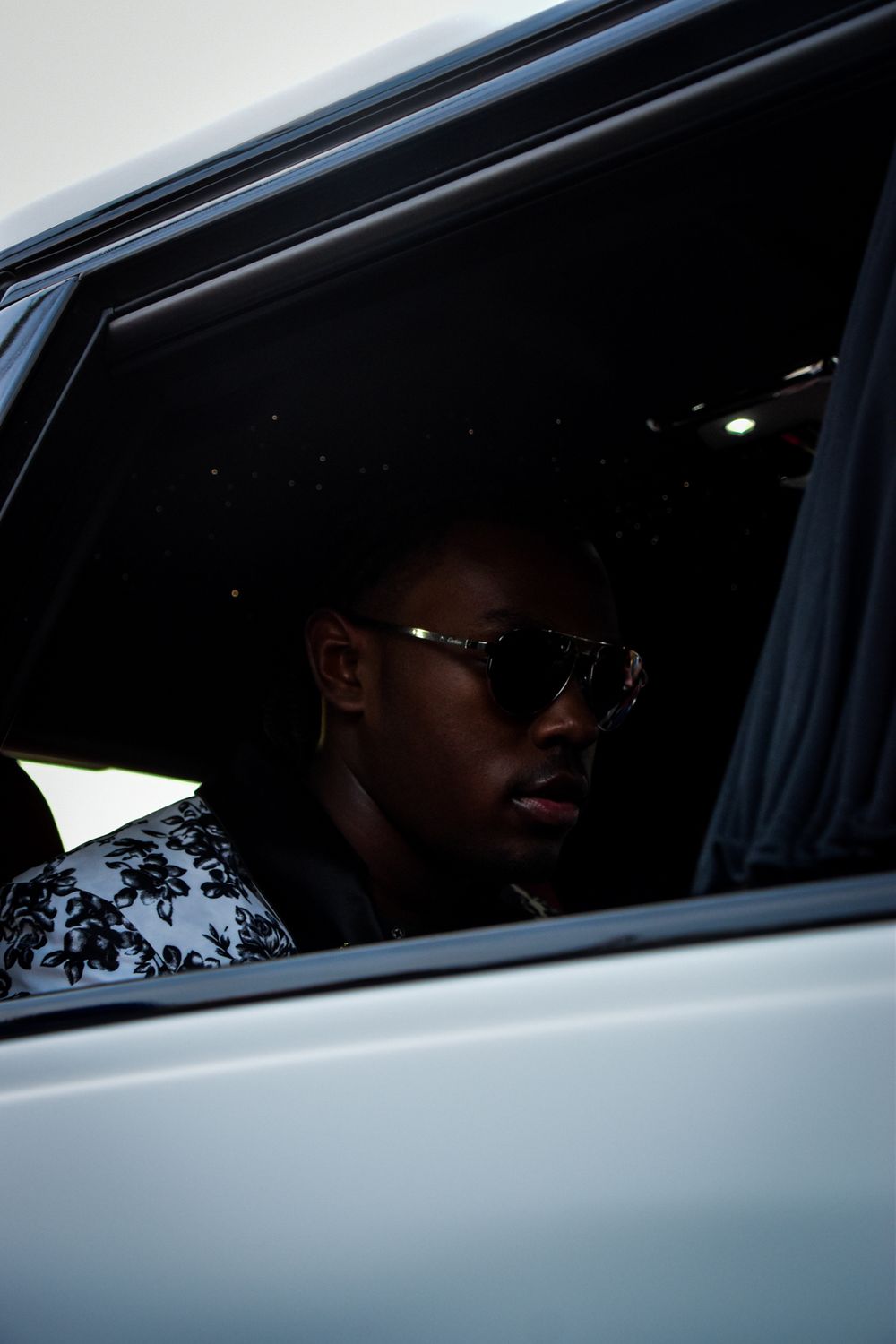 A silhouetted figure is visible through a car window against a dark background.