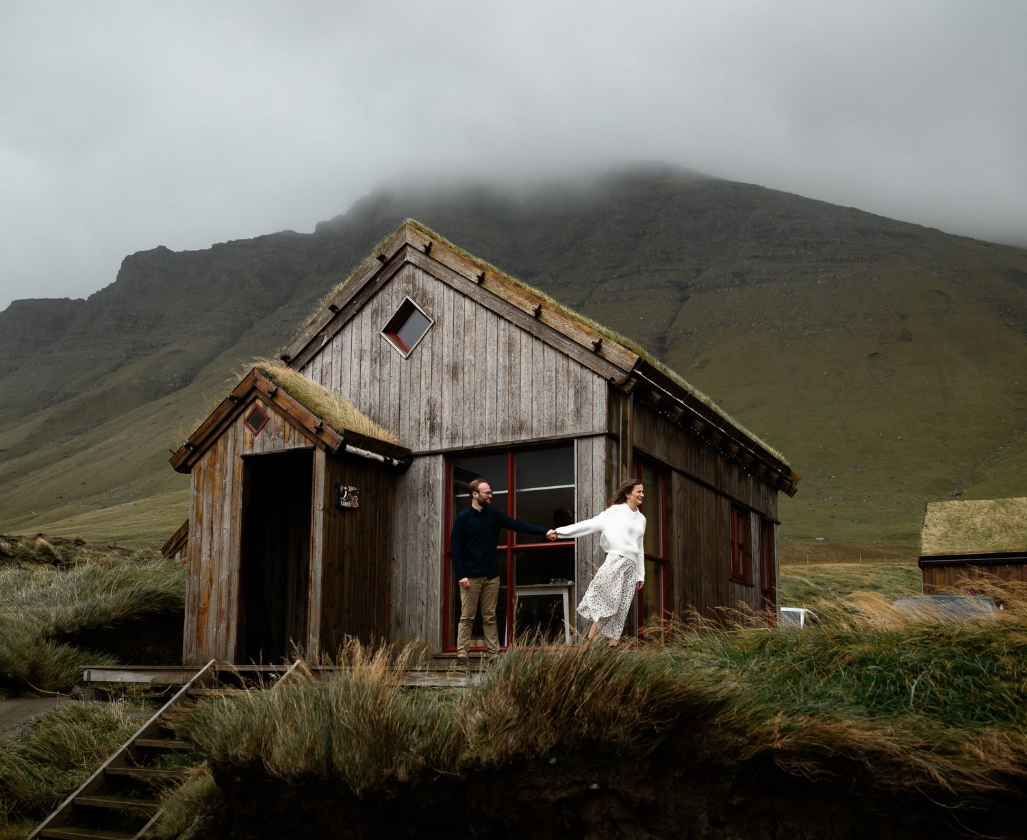 A rustic wooden cabin stands against misty mountain slopes in a remote wilderness setting.