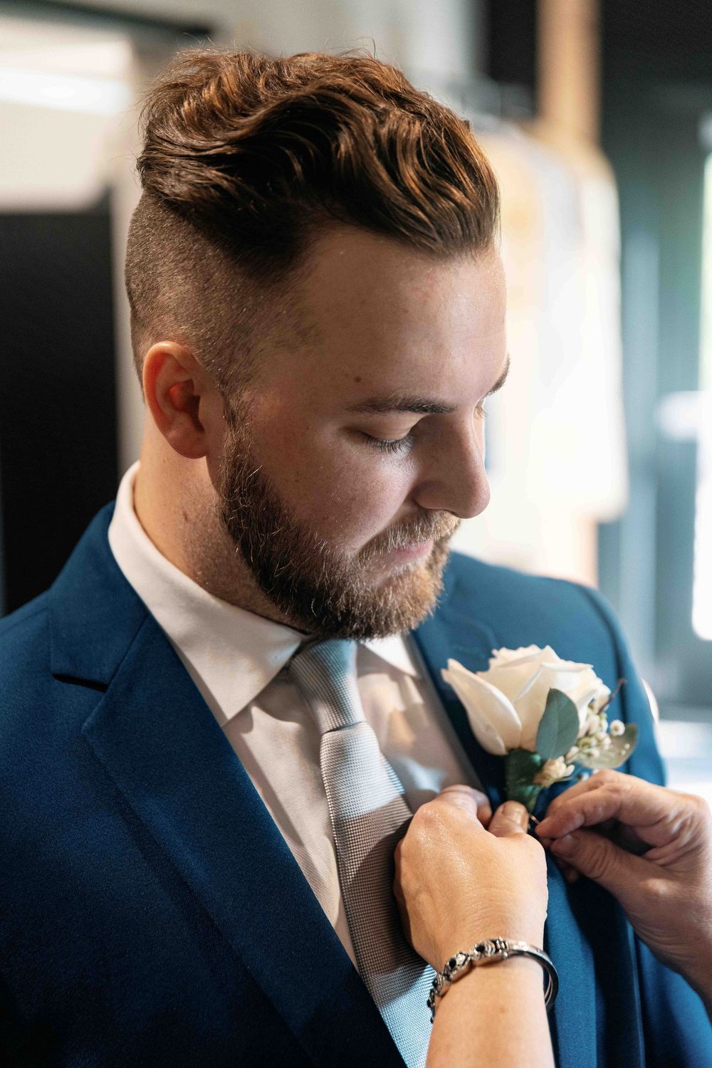 Portrait of groom getting boutonniere pinned.