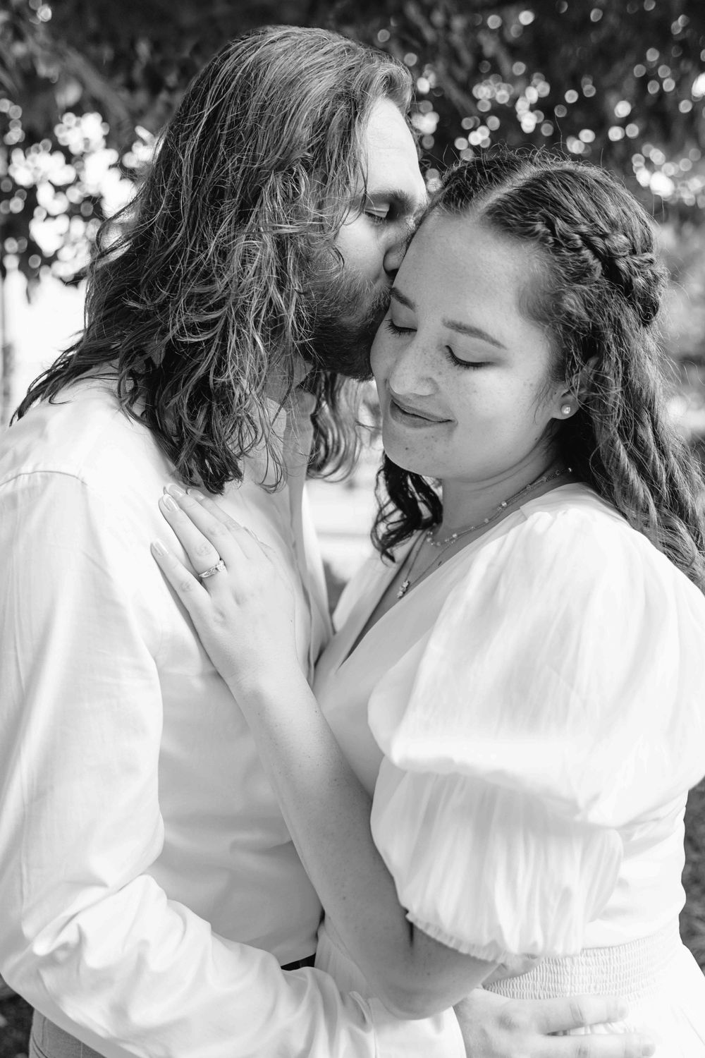 Black and white image of an engaged couple embracing outdoors.