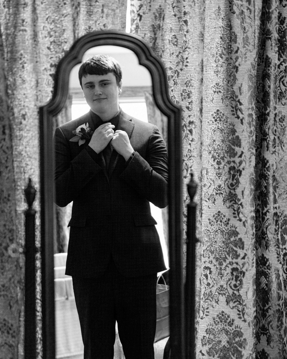 Portrait of groom straightening tie in mirror.