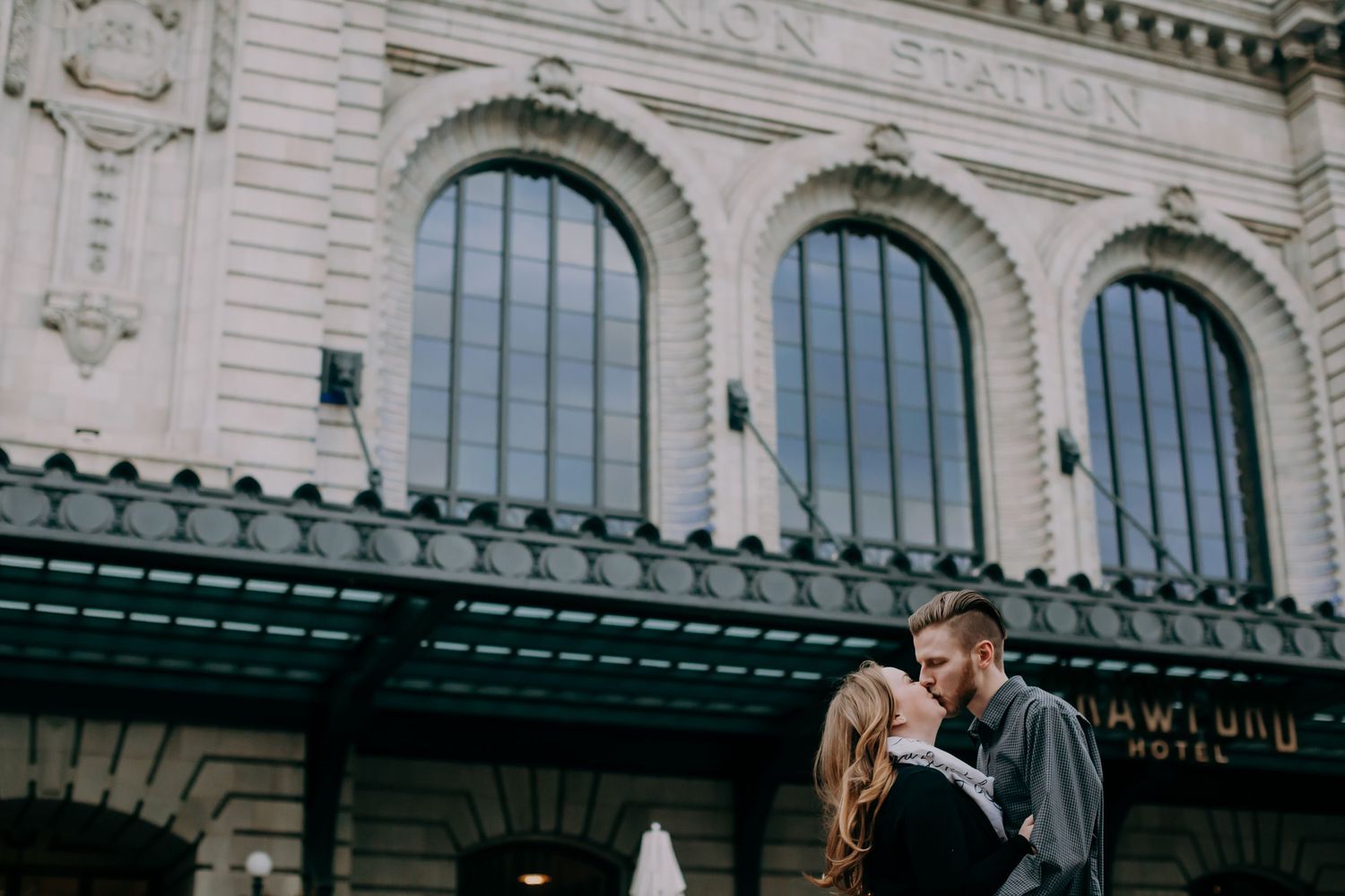Couple sharing a romantic kiss in front of a historic Union Station building facade.