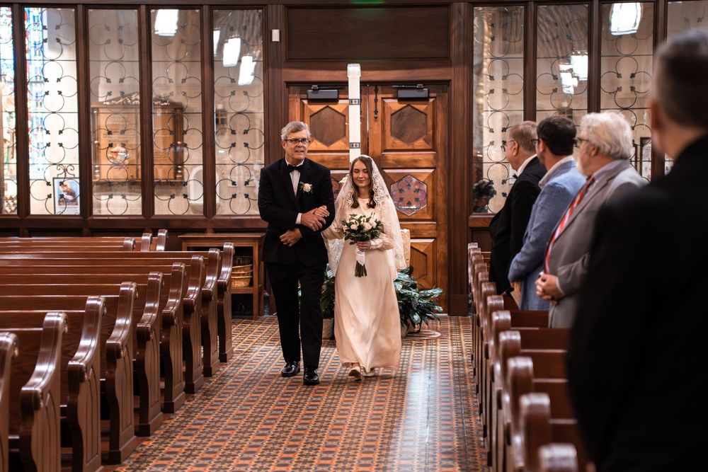 A wedding ceremony in progress at a traditional church with wooden pews and stained glass windows.