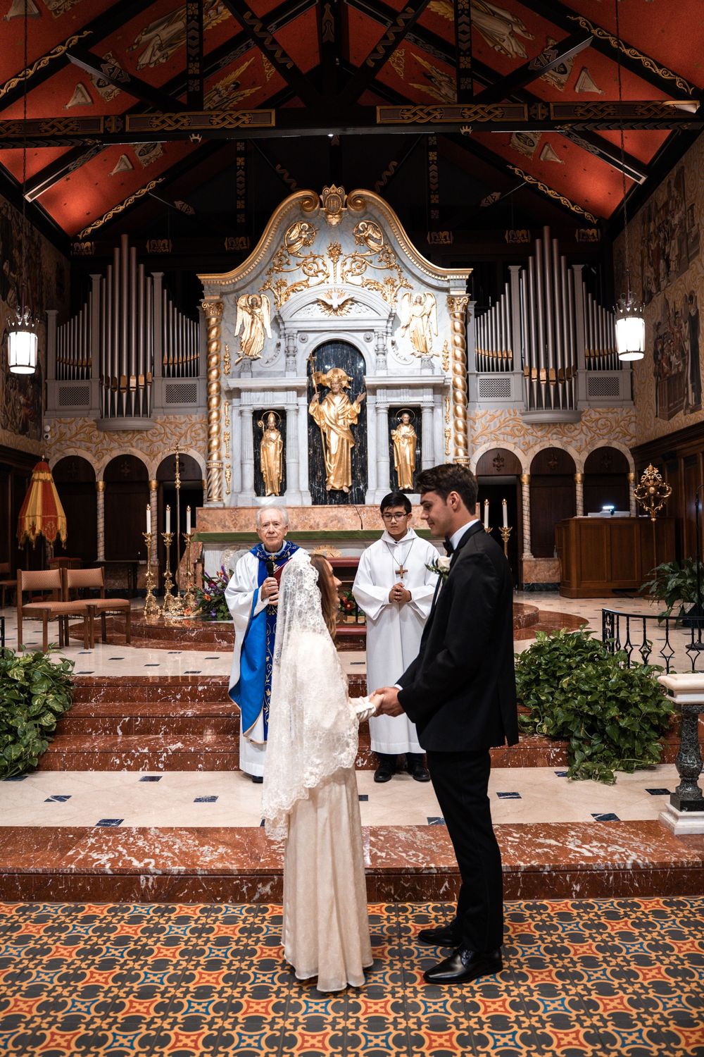 A wedding ceremony takes place in an ornate church with a pipe organ and decorative altar.
