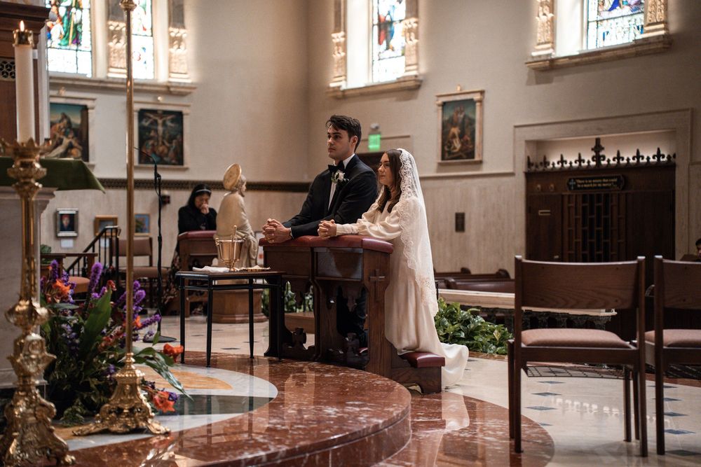 A church interior with stained glass windows, wooden pews, and people gathered for a wedding ceremony.