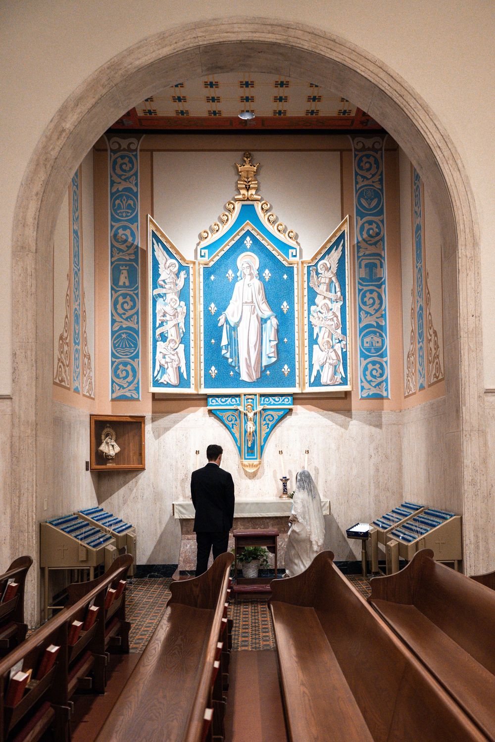 A church altar with blue and white religious artwork displayed in arched panels and wooden pews in the foreground.