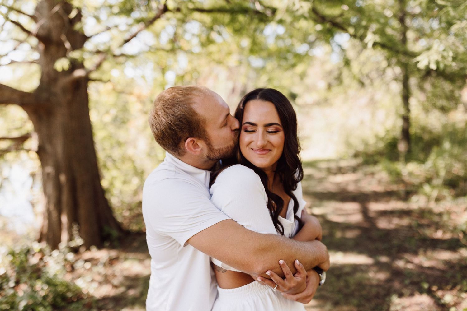 Romantic couple embracing under blooming spring trees in a sunlit outdoor setting.